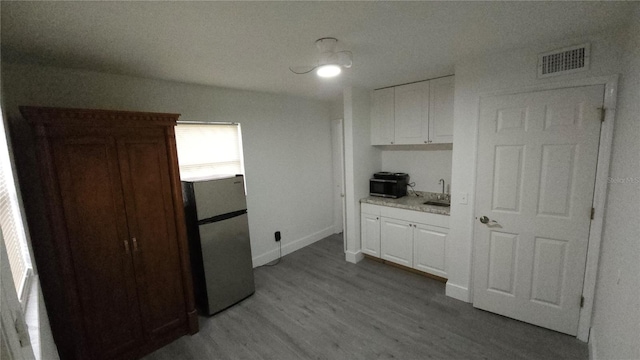 kitchen featuring freestanding refrigerator, visible vents, a sink, and white cabinetry