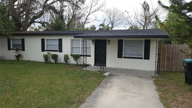 single story home with a shingled roof, fence, concrete block siding, and a front lawn