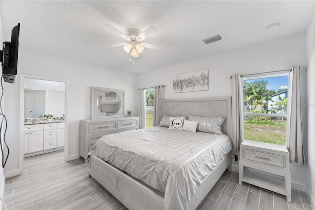 bedroom with ceiling fan, ensuite bath, and a textured ceiling