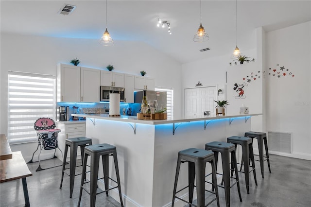 kitchen featuring concrete flooring, hanging light fixtures, stainless steel appliances, and white cabinets