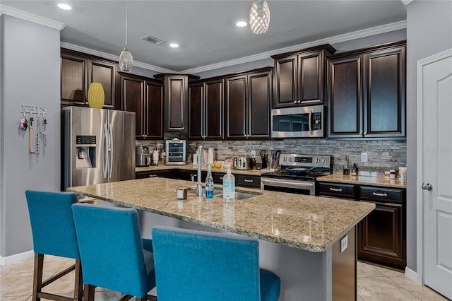 kitchen featuring stainless steel appliances, hanging light fixtures, a breakfast bar area, and a center island with sink