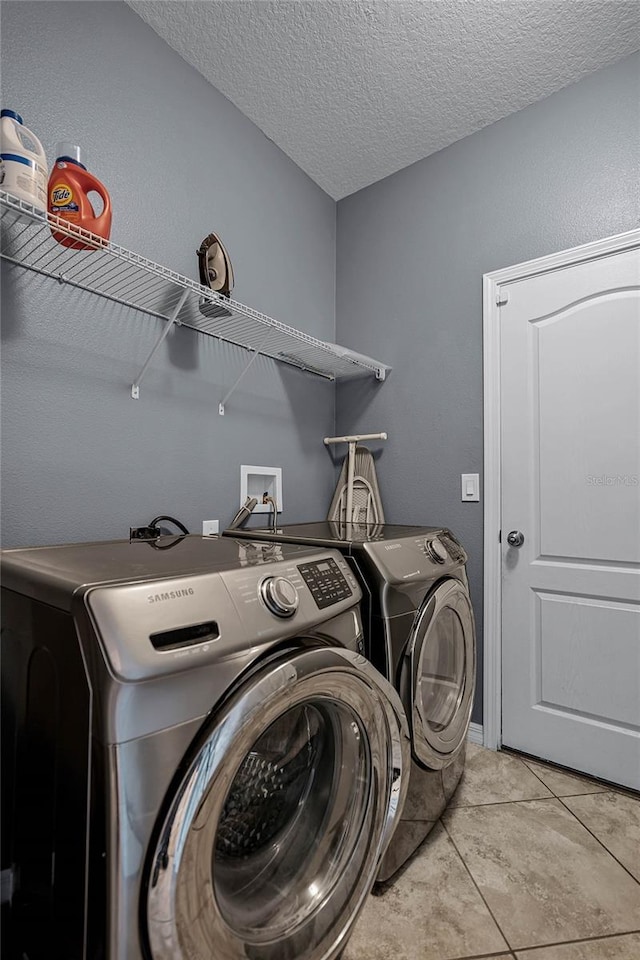 washroom with washing machine and dryer, light tile patterned floors, and a textured ceiling