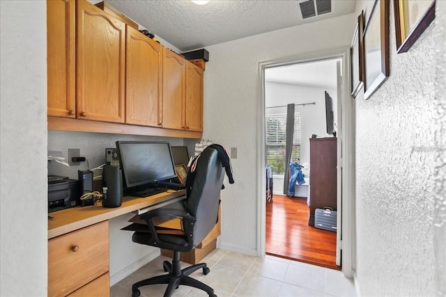 office with built in desk, a textured ceiling, and light tile patterned floors