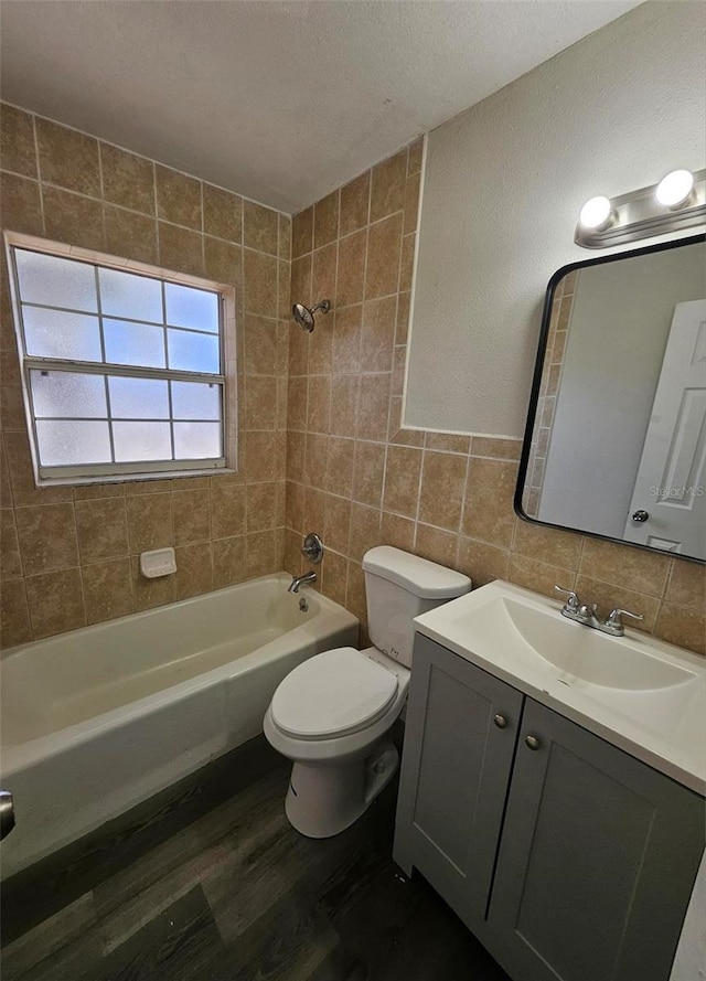 full bathroom with tiled shower / bath, tile walls, hardwood / wood-style flooring, vanity, and toilet