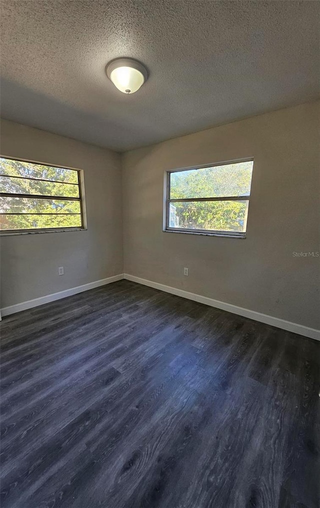 empty room with dark hardwood / wood-style flooring, plenty of natural light, and a textured ceiling