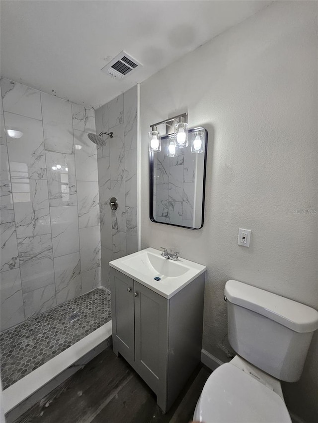 bathroom with vanity, wood-type flooring, a tile shower, and toilet