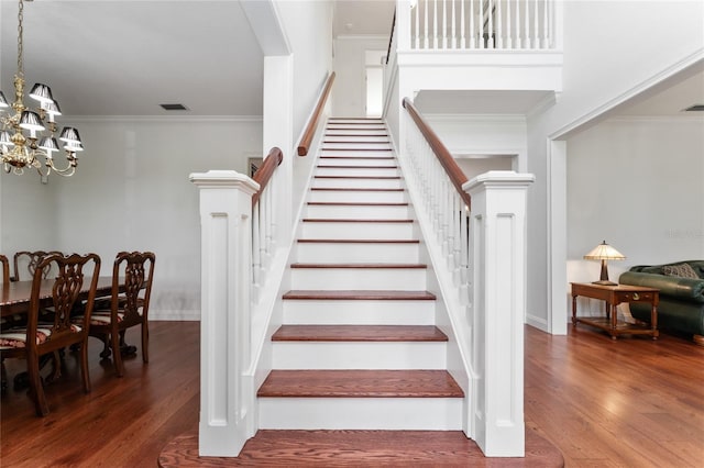 stairs featuring hardwood / wood-style flooring, ornamental molding, and a notable chandelier