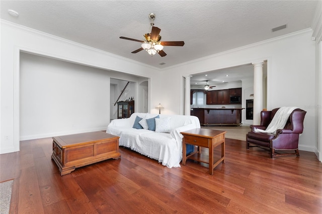 living room with ornate columns, ornamental molding, ceiling fan, dark wood-type flooring, and a textured ceiling