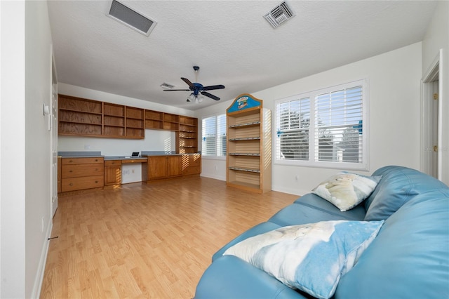 living room with ceiling fan, built in desk, a textured ceiling, and light hardwood / wood-style flooring