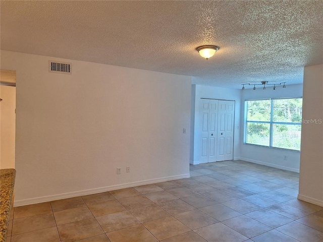 empty room featuring rail lighting, a textured ceiling, and light tile patterned floors