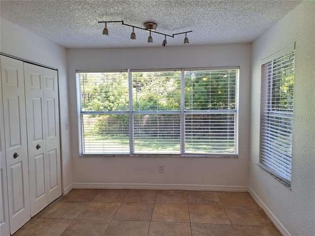 interior space featuring tile patterned flooring, rail lighting, and a textured ceiling