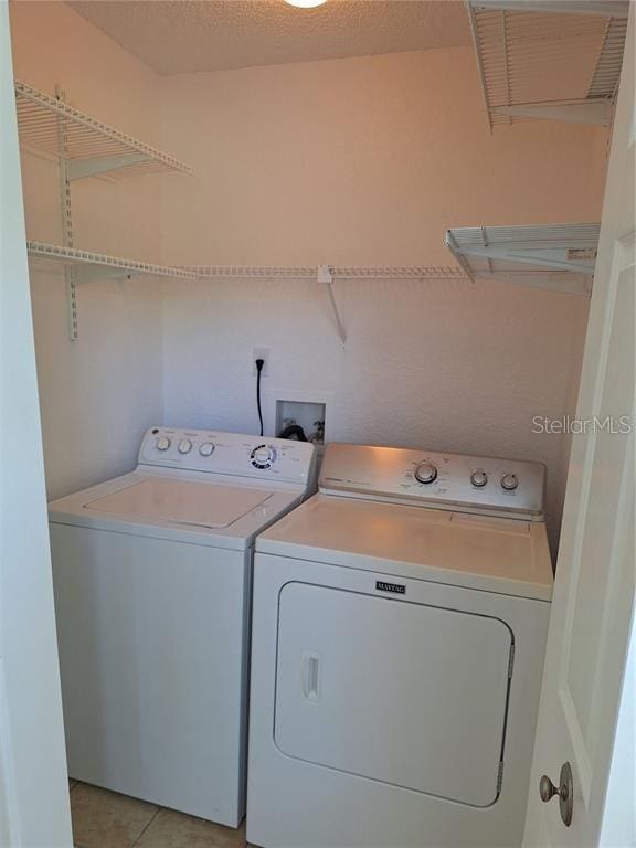 laundry room featuring light tile patterned floors, washing machine and dryer, and a textured ceiling