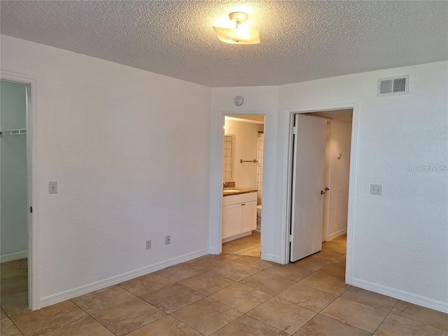 unfurnished bedroom with a walk in closet, ensuite bath, a textured ceiling, light tile patterned floors, and a closet