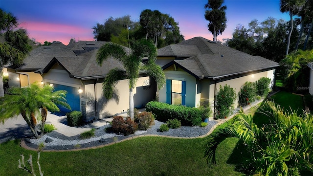 view of front facade featuring a garage, roof with shingles, a front lawn, and stucco siding