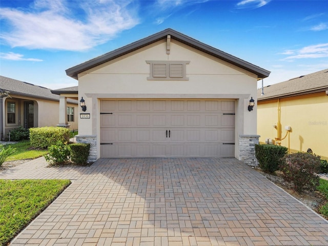 view of front of house with decorative driveway, stone siding, a garage, and stucco siding