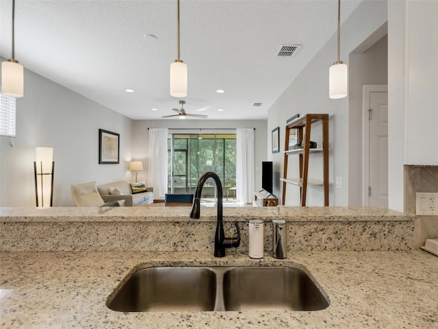 kitchen with decorative light fixtures, visible vents, open floor plan, a sink, and light stone countertops