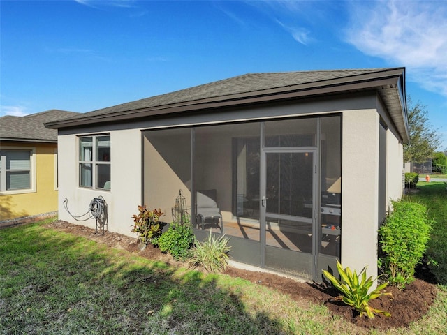 back of house featuring a sunroom, a lawn, and stucco siding