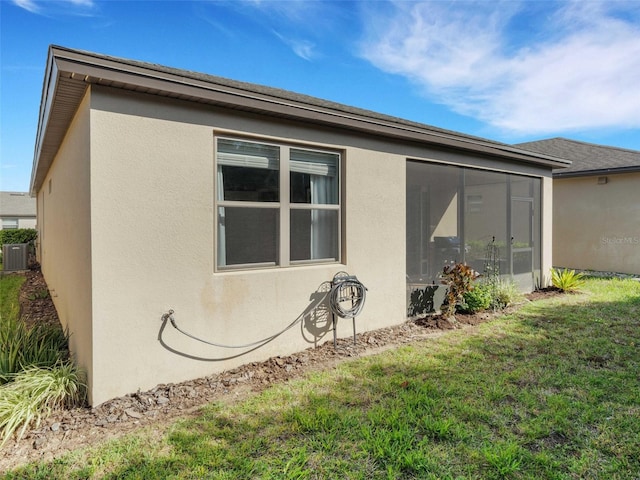 view of side of home featuring a sunroom, cooling unit, a lawn, and stucco siding