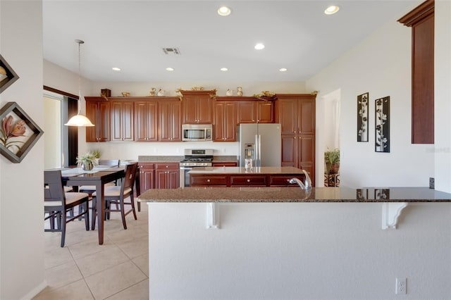 kitchen featuring appliances with stainless steel finishes, pendant lighting, a kitchen bar, and dark stone counters