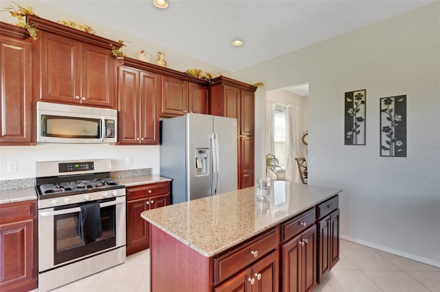 kitchen with appliances with stainless steel finishes, light tile patterned flooring, light stone countertops, and a center island