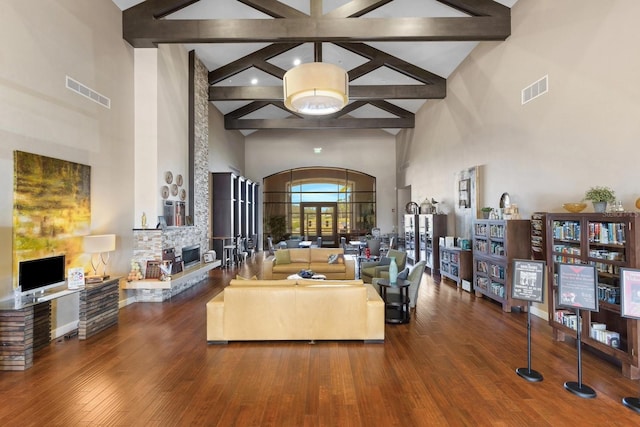 living room featuring beam ceiling, high vaulted ceiling, a stone fireplace, and hardwood / wood-style floors