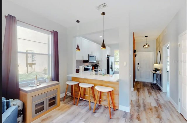 kitchen with a breakfast bar, pendant lighting, white cabinetry, kitchen peninsula, and stainless steel appliances