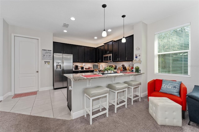 kitchen with appliances with stainless steel finishes, hanging light fixtures, tasteful backsplash, light stone counters, and kitchen peninsula