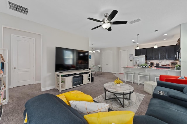 carpeted living room with ceiling fan with notable chandelier