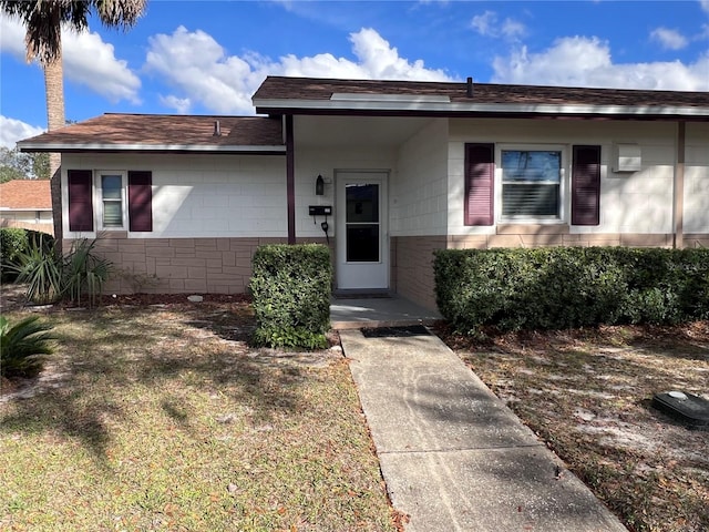 single story home with a front yard, concrete block siding, and roof with shingles