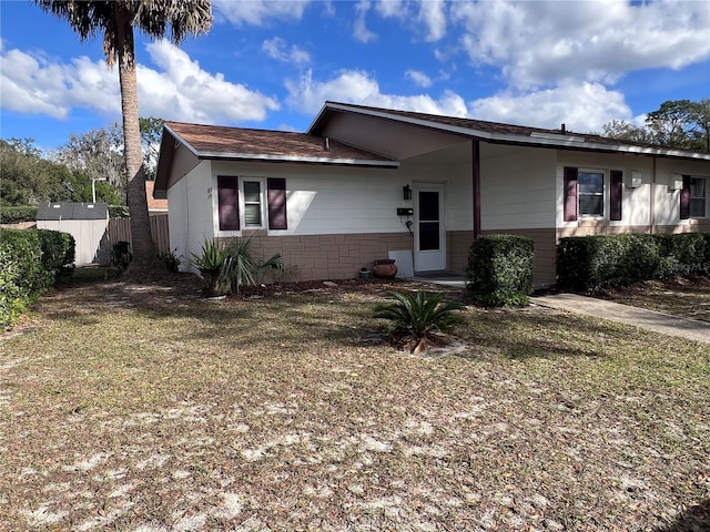 ranch-style house featuring fence, concrete block siding, and a front lawn