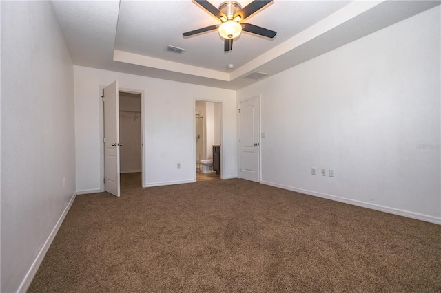 unfurnished bedroom with connected bathroom, a walk in closet, carpet flooring, a tray ceiling, and a closet