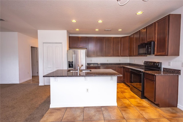 kitchen with sink, dark stone countertops, light colored carpet, a kitchen island with sink, and black appliances