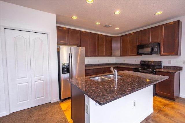 kitchen with sink, dark stone counters, black appliances, a center island with sink, and a textured ceiling