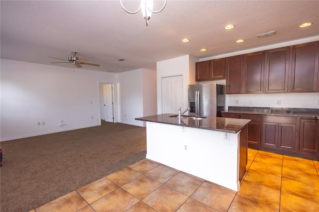 kitchen with sink, light carpet, a textured ceiling, stainless steel fridge, and an island with sink