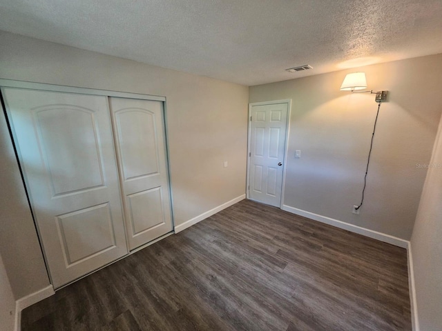 unfurnished bedroom featuring a textured ceiling, dark hardwood / wood-style flooring, and a closet