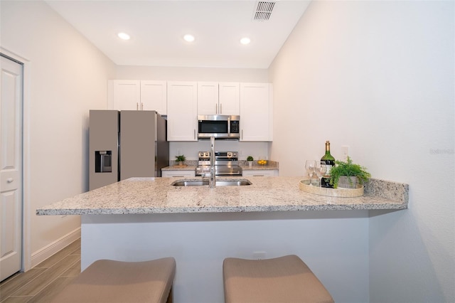 kitchen with a kitchen bar, appliances with stainless steel finishes, kitchen peninsula, light stone countertops, and white cabinets