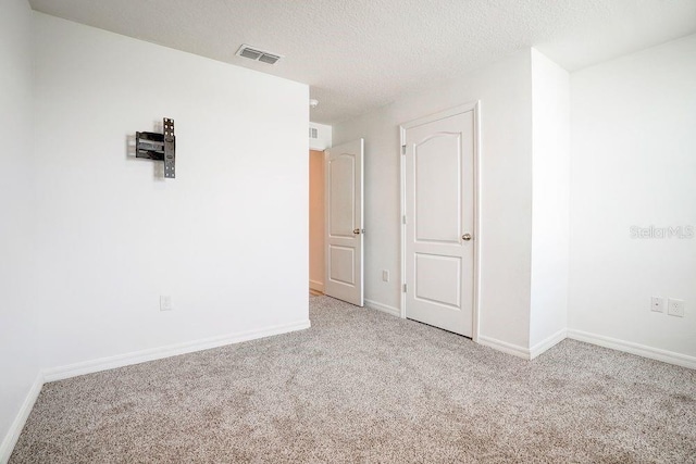 empty room with light colored carpet and a textured ceiling