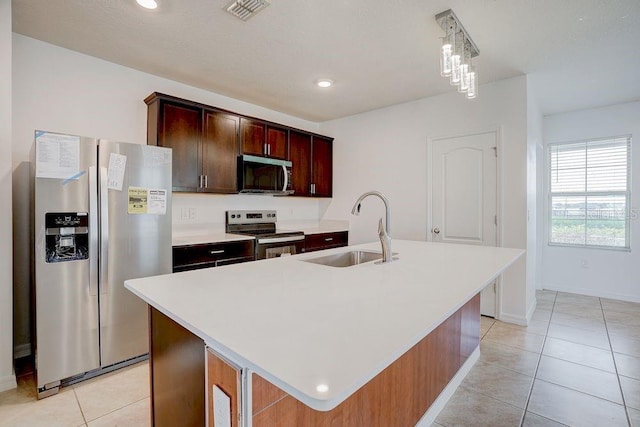 kitchen with light tile patterned flooring, decorative light fixtures, an island with sink, sink, and stainless steel appliances