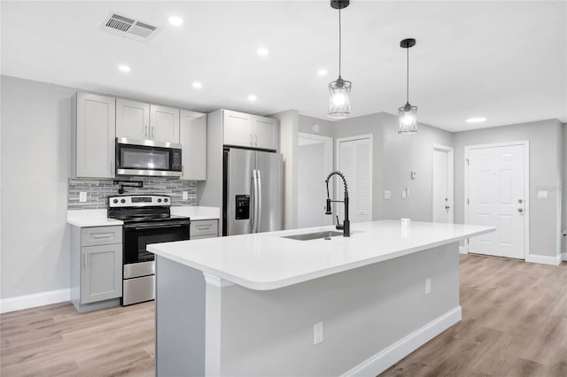 kitchen with gray cabinets, sink, hanging light fixtures, stainless steel appliances, and a center island with sink