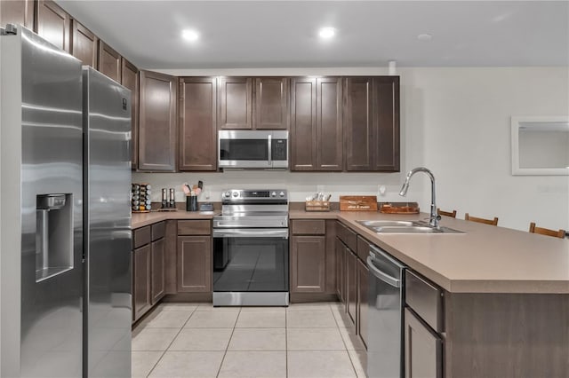 kitchen featuring dark brown cabinetry, sink, light tile patterned floors, appliances with stainless steel finishes, and kitchen peninsula