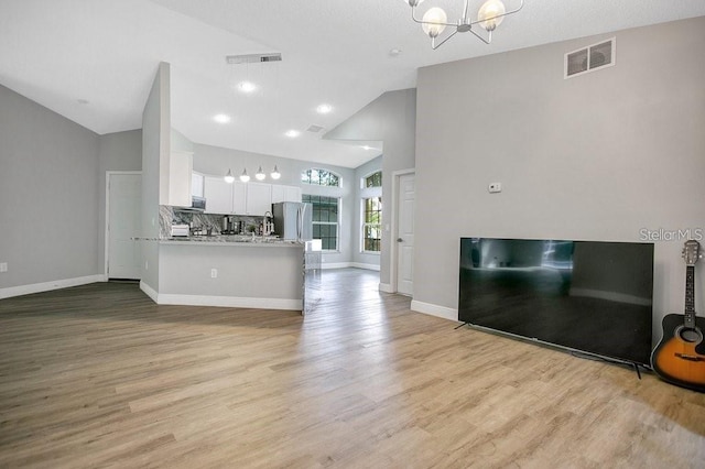 unfurnished living room featuring a chandelier, high vaulted ceiling, and light hardwood / wood-style flooring