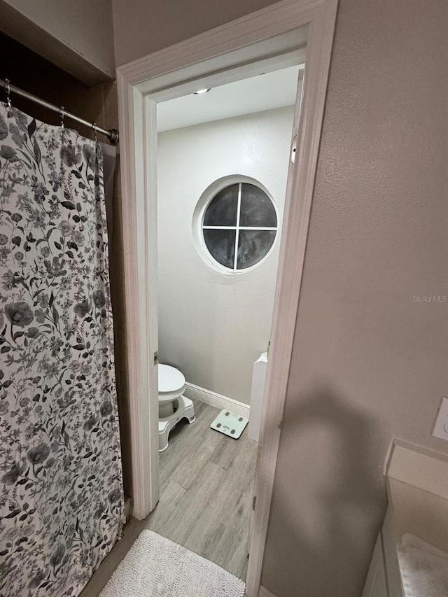 bathroom with toilet, curtained shower, and hardwood / wood-style floors