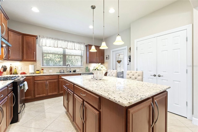 kitchen featuring a center island, pendant lighting, stainless steel range with gas cooktop, decorative backsplash, and light stone countertops