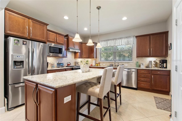 kitchen featuring decorative light fixtures, stainless steel appliances, decorative backsplash, a kitchen island, and light stone countertops