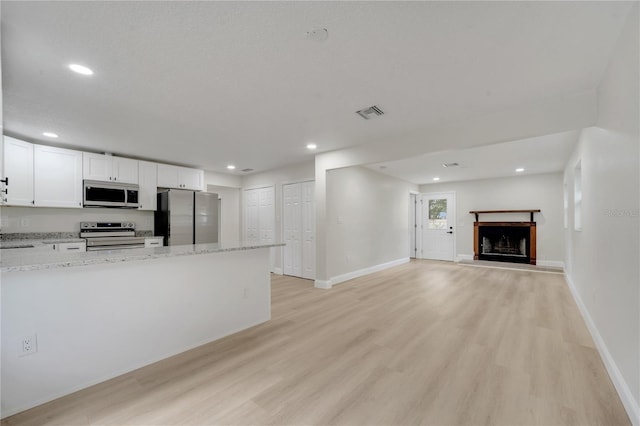 kitchen with white cabinetry, appliances with stainless steel finishes, light stone counters, and light hardwood / wood-style flooring