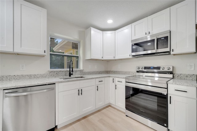 kitchen with stainless steel appliances, white cabinetry, light stone countertops, and sink