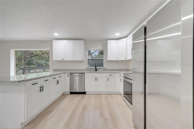 kitchen with sink, white cabinetry, light stone counters, stainless steel appliances, and light hardwood / wood-style floors