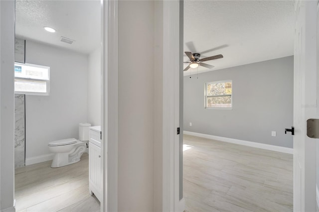 bathroom featuring ceiling fan, a healthy amount of sunlight, a textured ceiling, and toilet