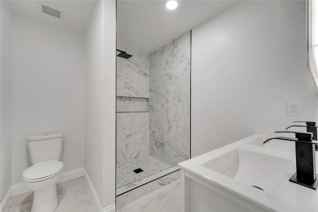 bathroom featuring tiled shower, toilet, and double sink