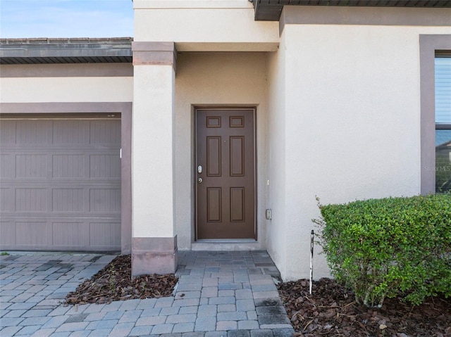 view of exterior entry featuring an attached garage and stucco siding